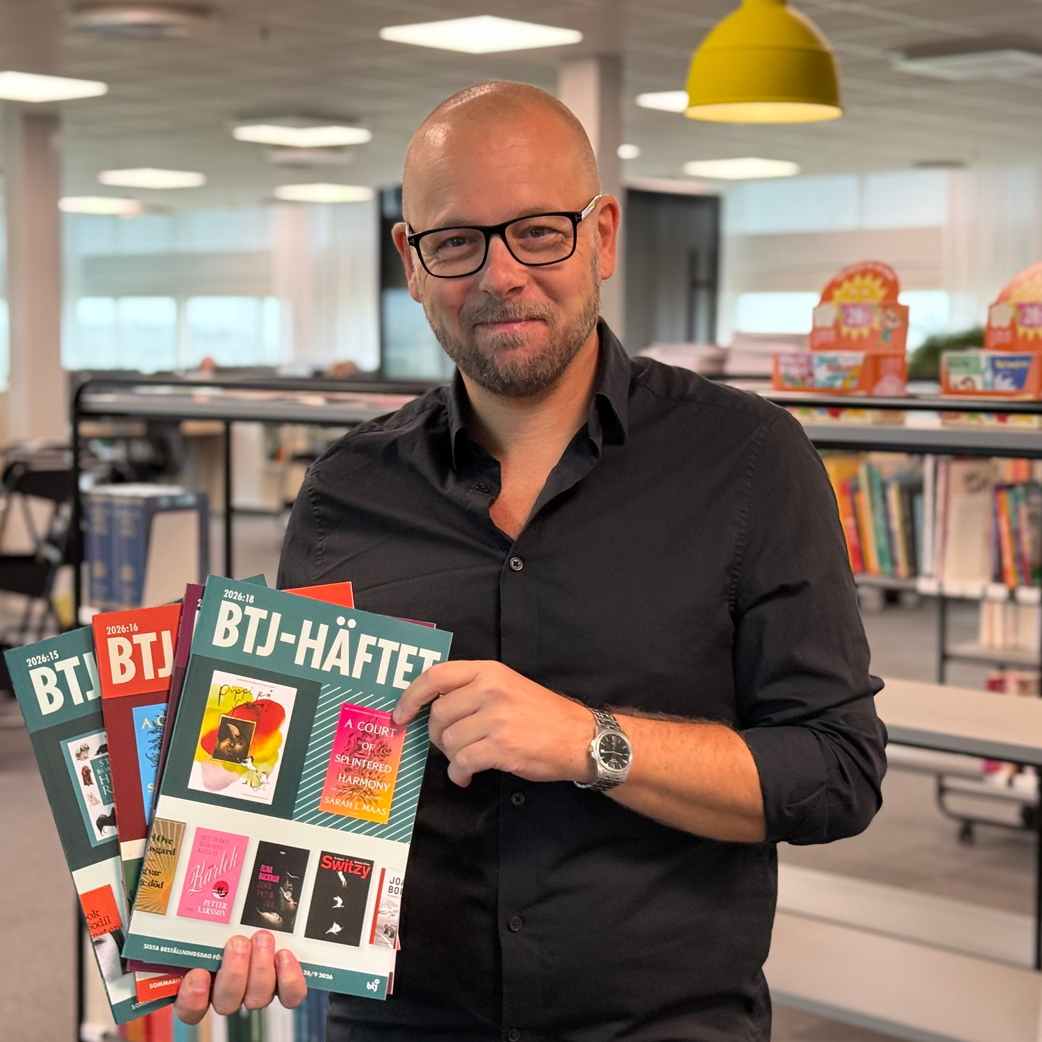 Man i svart skjorta med tre BTJ-häften i händerna.